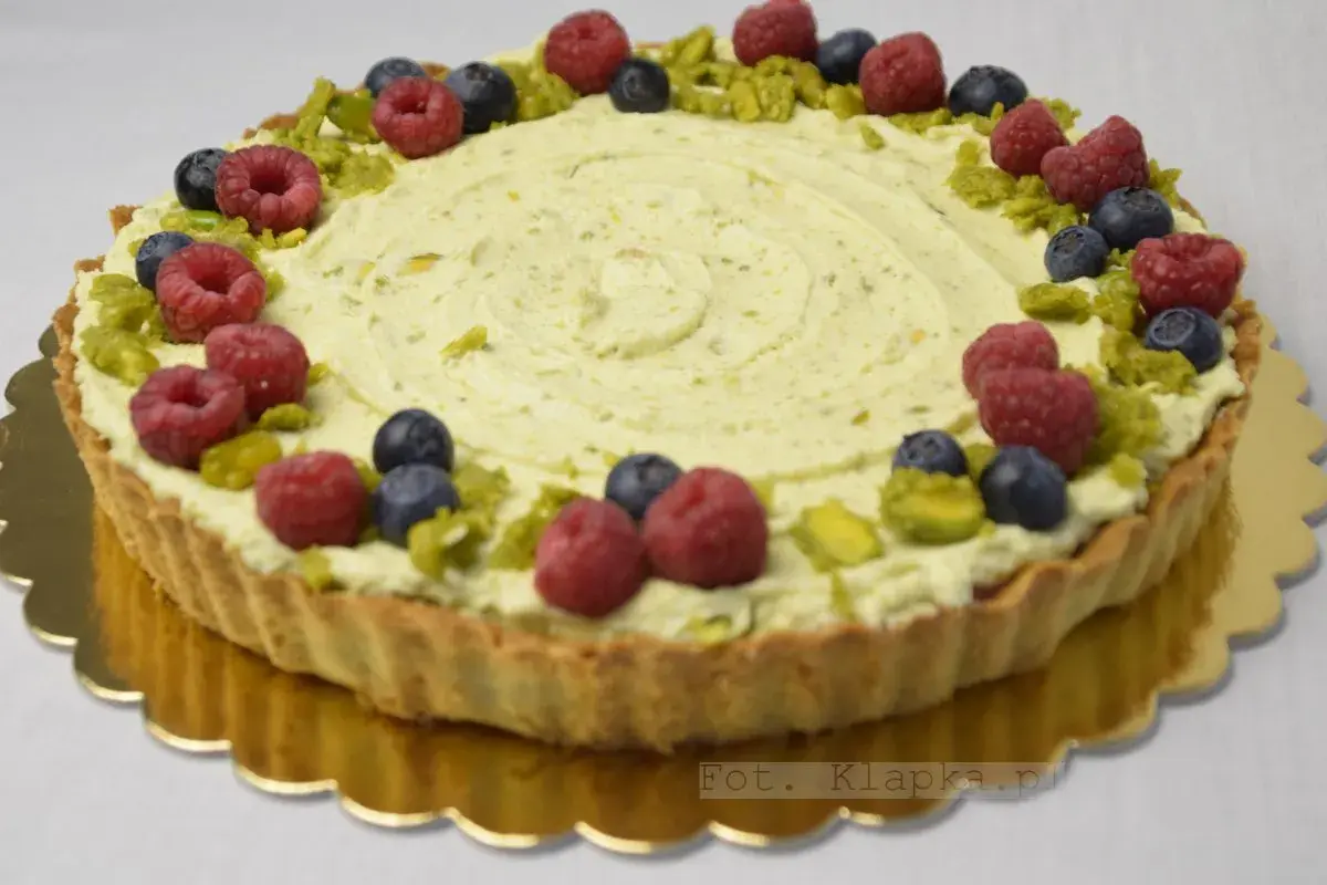 Tarta pistacjowa z białą czekoladą, ozdobiona malinami, borówkami i pistacjami.