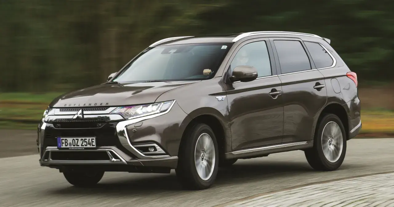 Brązowy Mitsubishi Outlander PHEV jedzie po drodze, z rozmytym tłem lasu.