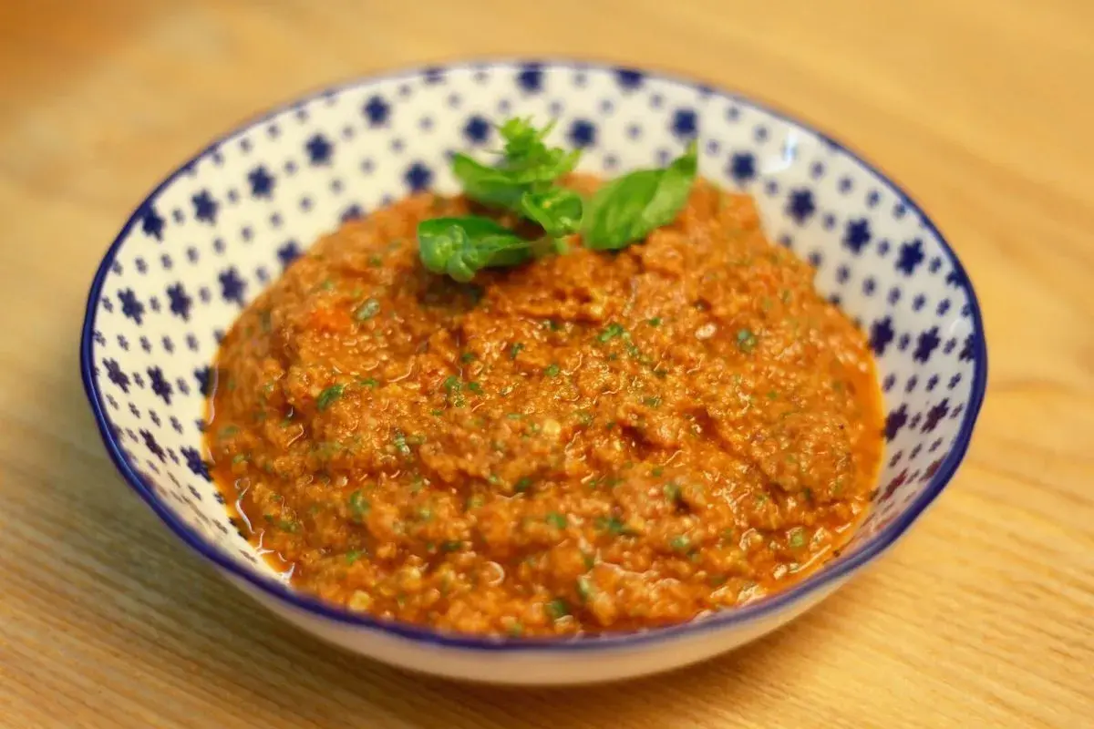 Un cuenco de pesto rosso casero, con hojas de albahaca fresca encima, listo para acompañar pasta o bruschetta.