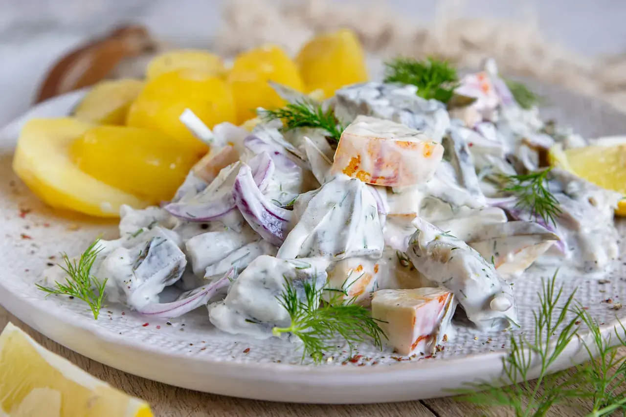Matjessalat Hausfrauenart mit Pellkartoffeln, Zwiebeln und Dill in cremiger Sauce, garniert mit Zitronenspalten.