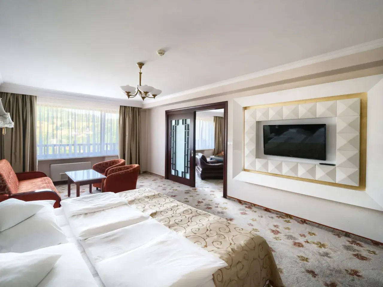 Pokój w hotelu Gołębiewski Wisła: wygodne łóżko, salonik z fotelami i kanapą, telewizor na ozdobnej ścianie.