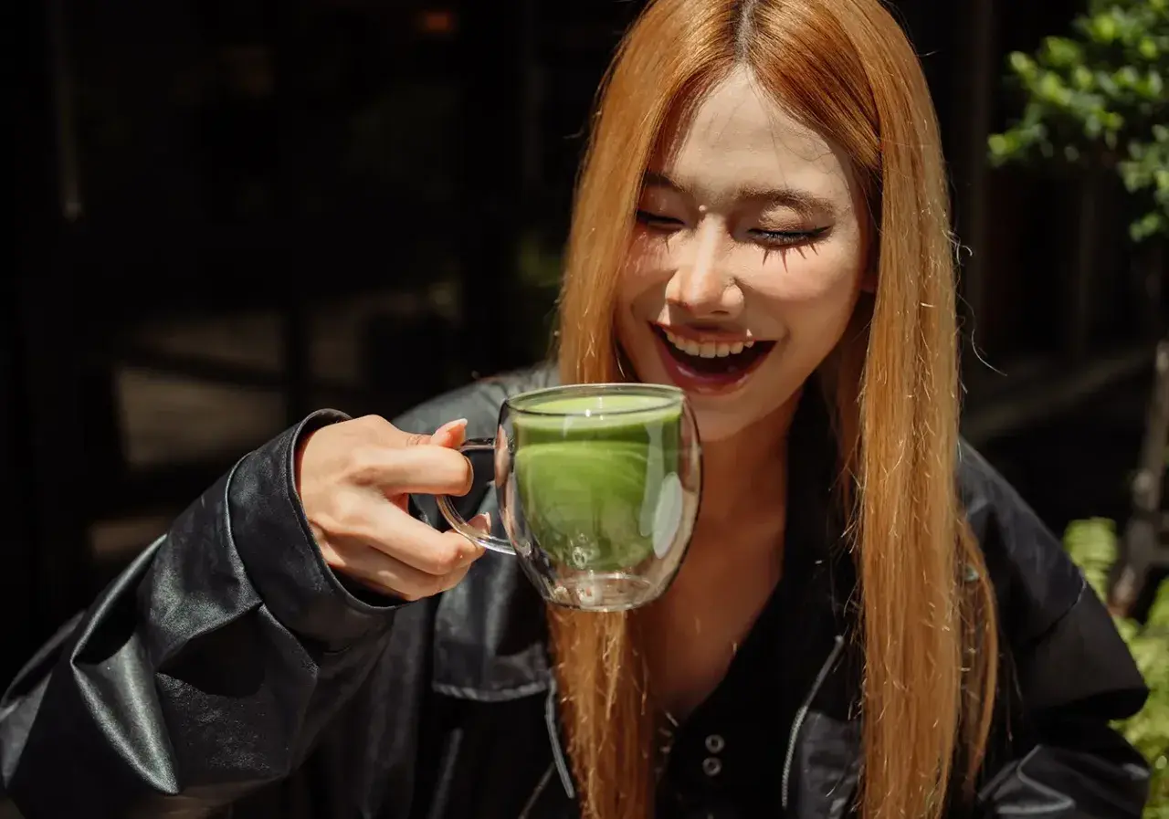 Lachende Frau hält eine Tasse Matcha. Mögliche matcha nebenwirkungen sind hier nicht sichtbar.