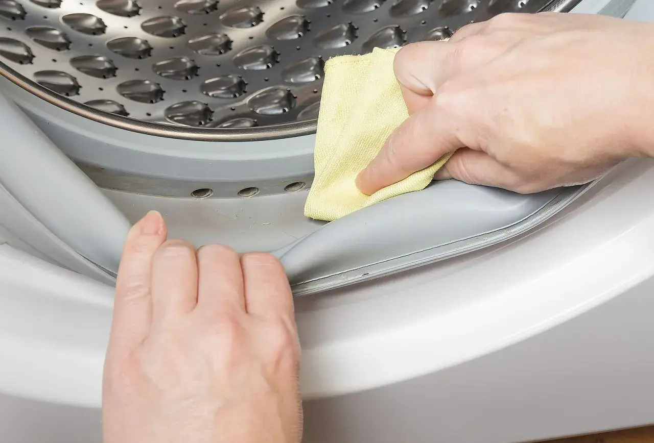 Manos limpian la goma de la lavadora con un paño amarillo para saber como quitar el mal olor de la lavadora.