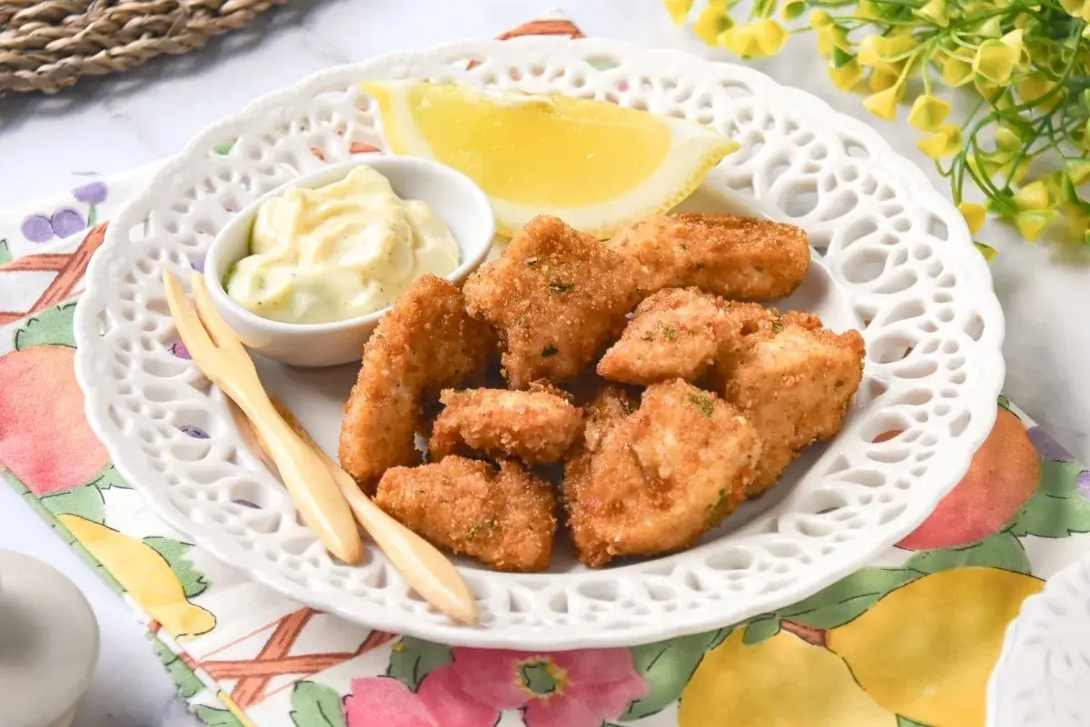 Deliciosas lagrimitas de pollo crujientes, servidas con mayonesa y limón en un plato blanco.