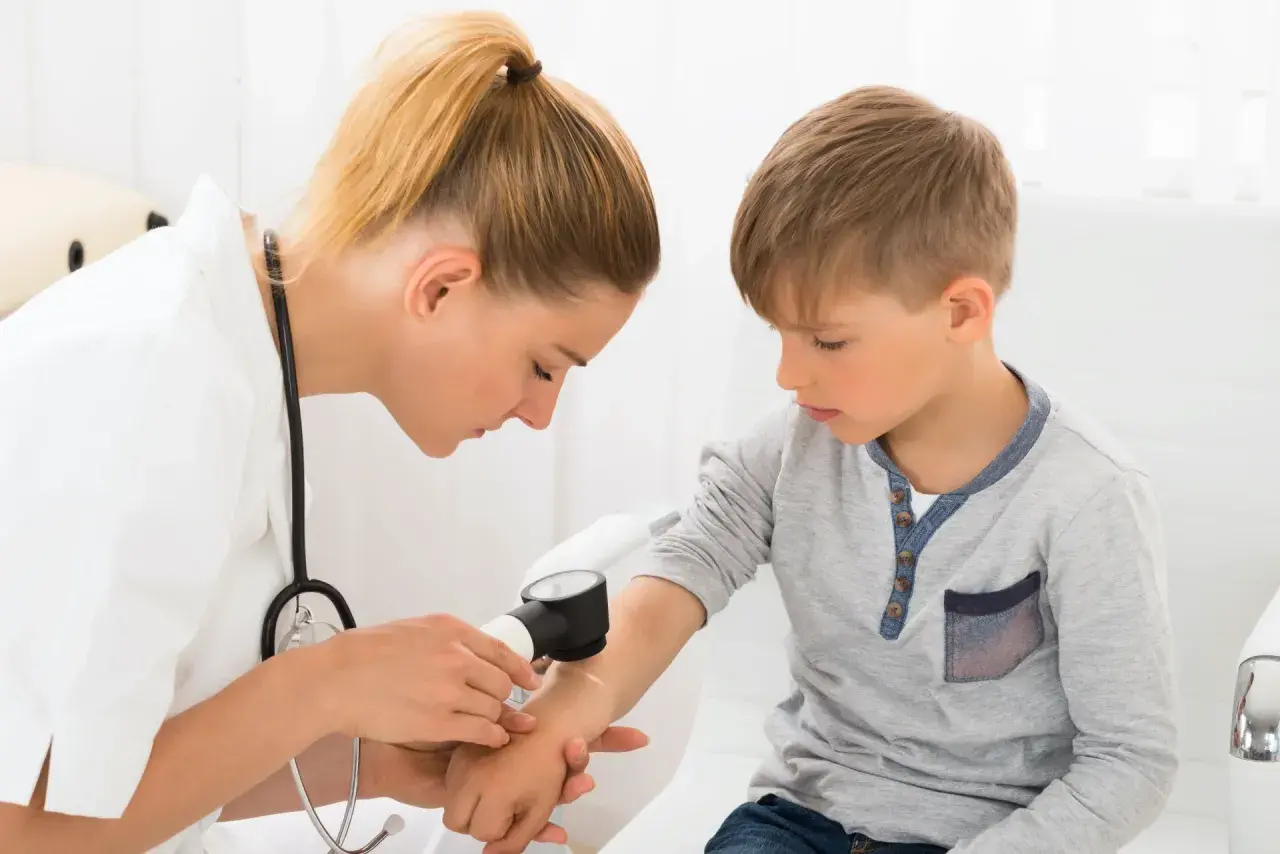 Lekarka bada rękę chłopca dermatoskopem, sprawdzając znamię dysplastyczne.