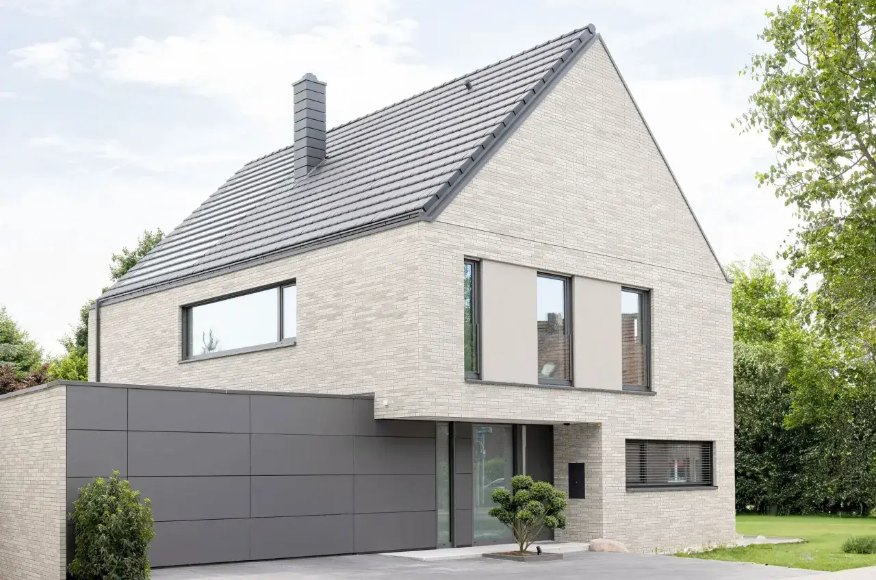 Modernes Haus mit hellem Klinker, das nicht gestrichen ist. Graues Dach, Garage und Fensterrahmen.