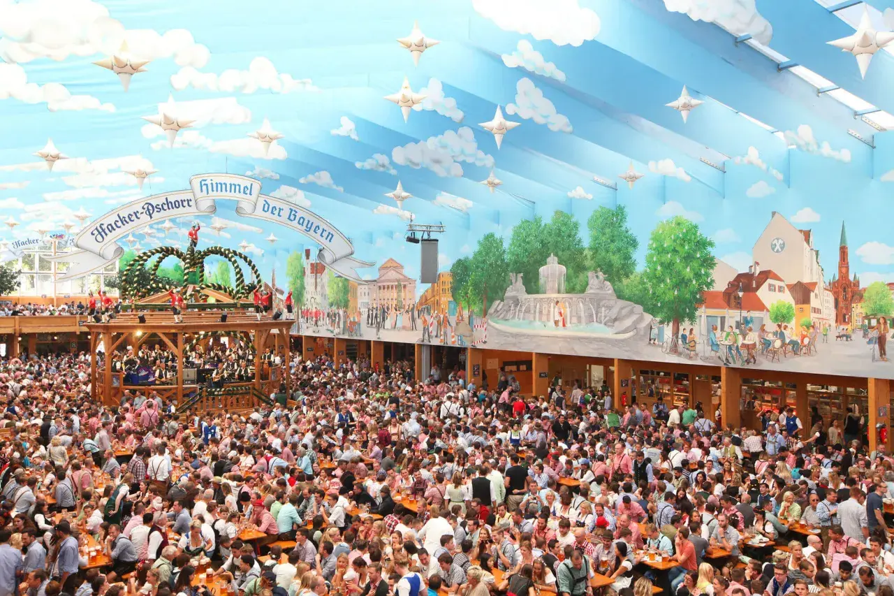 Folla festante in una tenda decorata con cielo azzurro e nuvole, un'autentica scena delle **tedesche Oktoberfest**.