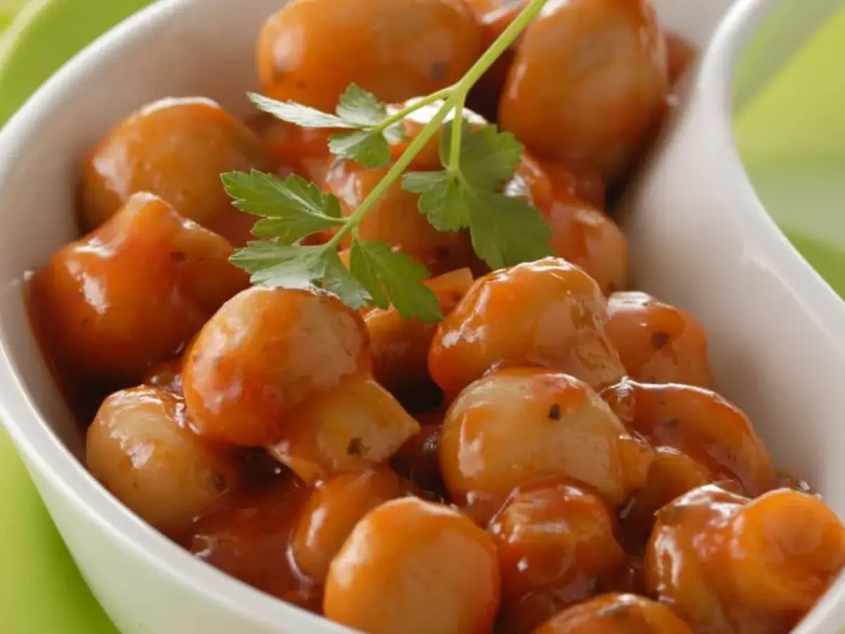 Champignons à la grecque, petits et tendres, nappés d'une sauce savoureuse et garni d'une feuille de persil.
