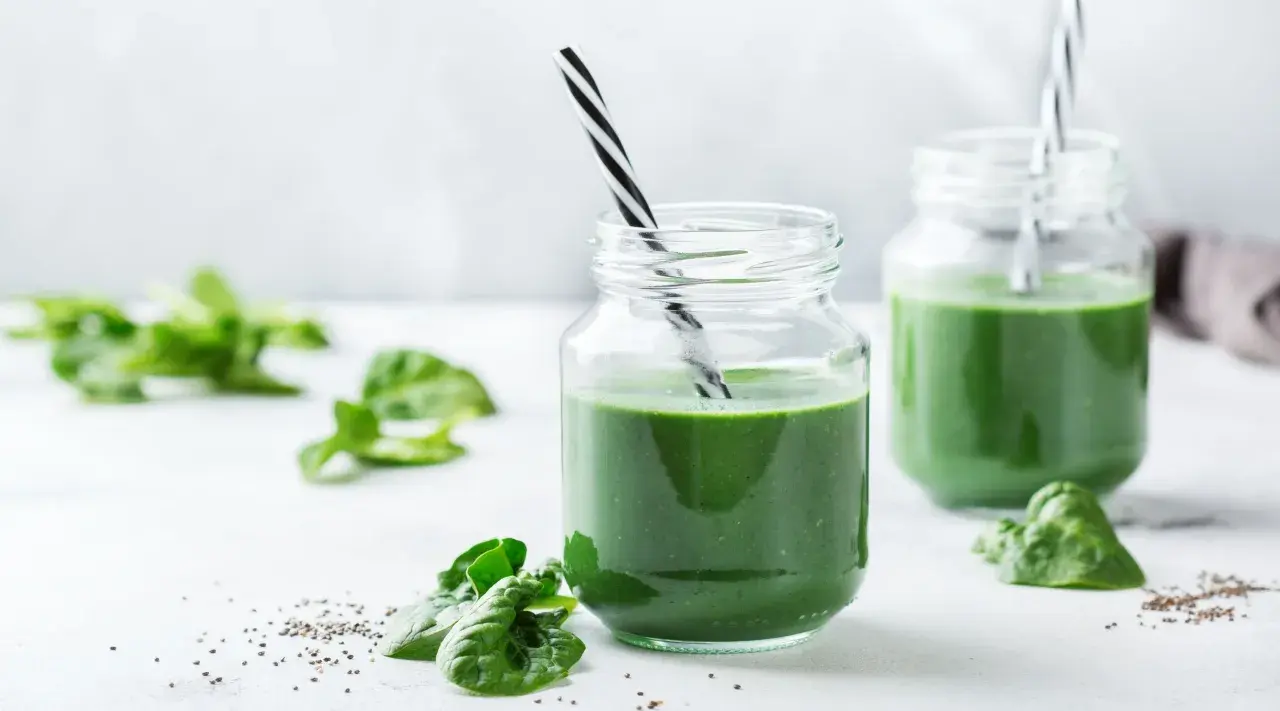 Två glas med grön smoothie, garnerade med spenatblad och chiafrön. Tänk på eventuella spirulina biverkningar innan du dricker.