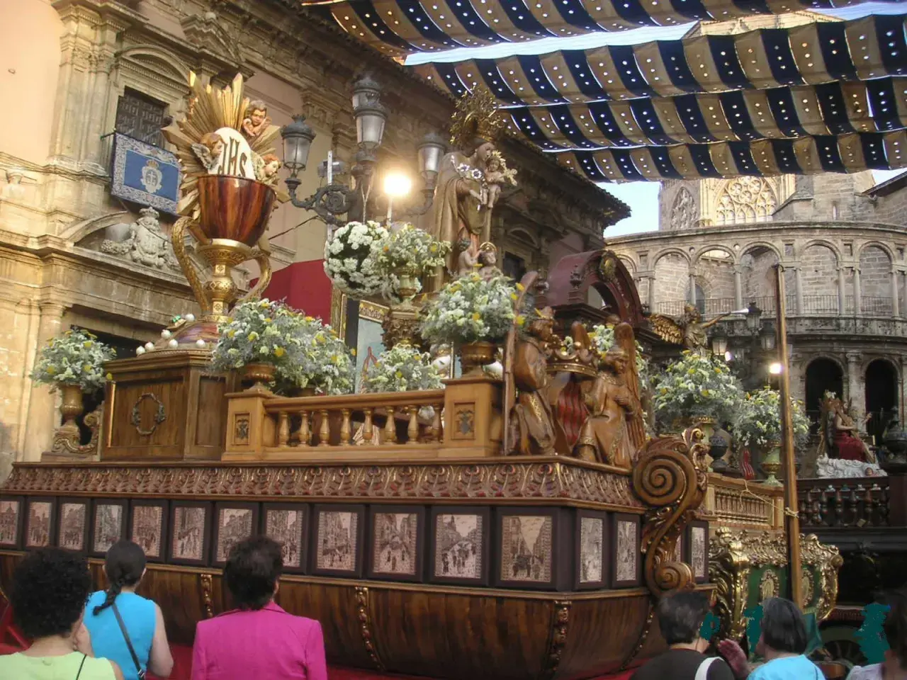 Procesión religiosa con un elaborado trono de madera adornado con flores y figuras. El **corpus 2026** se prepara para la festividad.