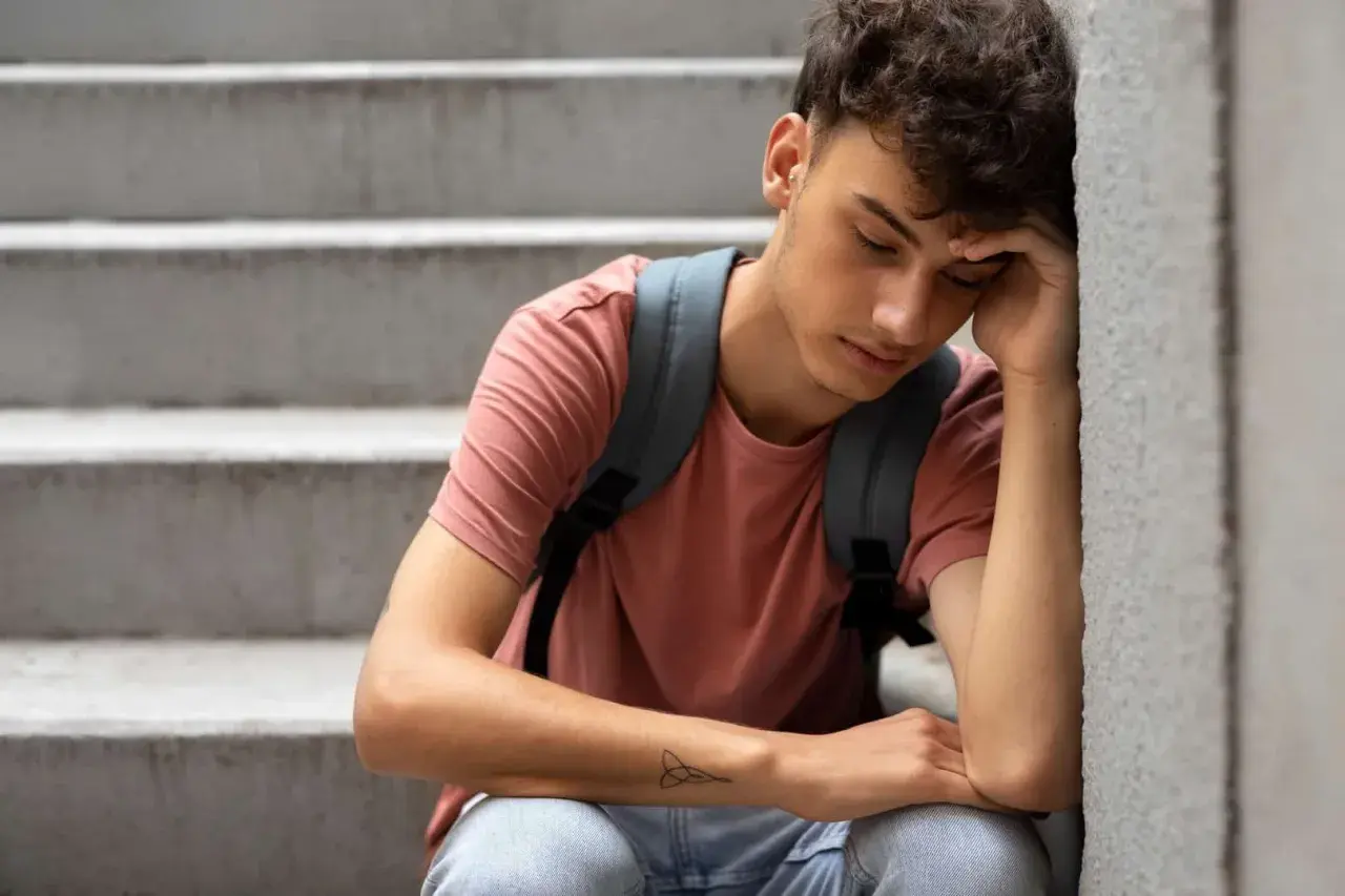 Młody chłopak siedzi na schodach, opierając głowę na dłoni. Wygląda na przygnębionego, jakby zastanawiał się, czym jest **demoralizacja**.