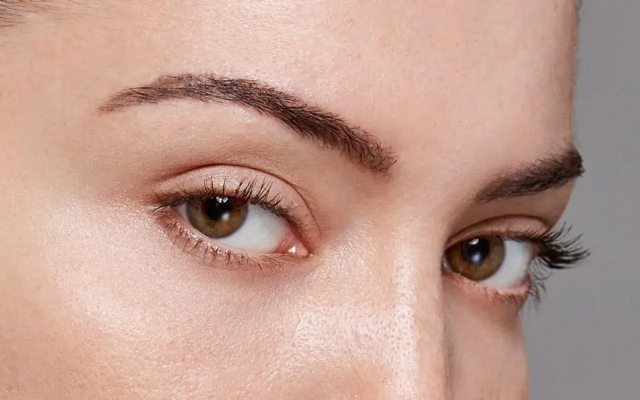 Gros plan sur des yeux marron avec des cils longs. Le sourcil gauche est légèrement plus fin, montrant comment dessiner ses sourcils pour un look naturel.