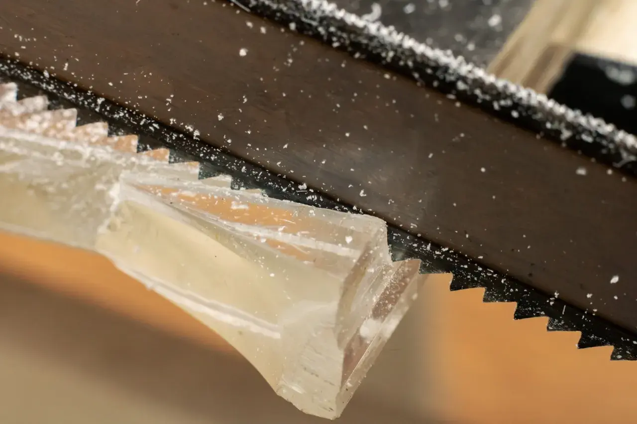 Sågtänder skär genom ett tjockt, genomskinligt material. Små bitar av kapa plexiglas flyger runt.