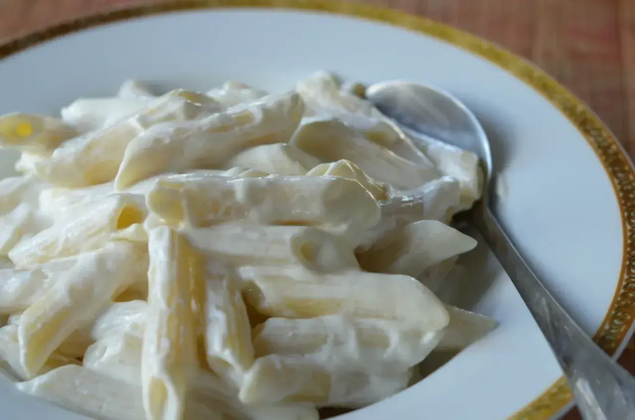 Penne z kremowym twarogiem na słodko, podane na talerzu z łyżką. Pyszne danie, które z pewnością zadowoli każdego.