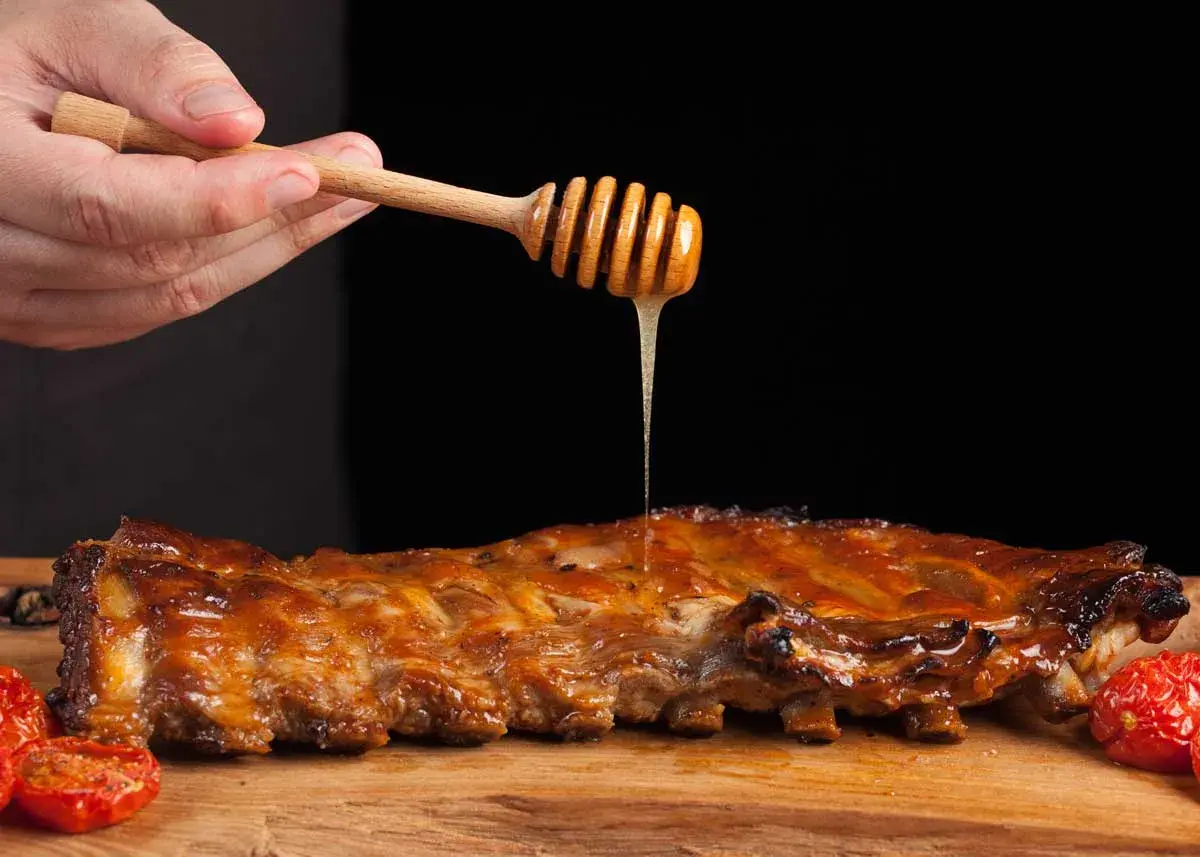 Costillas a la miel jugosas, bañadas con miel dorada de un palillo de madera. Acompañadas de tomates asados.