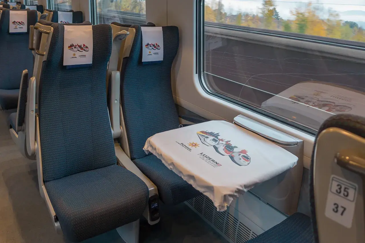 Sitze in einem ece train mit Kopfstützen und einem Tisch, der mit einem Tuch mit Zugmotiven bedeckt ist.