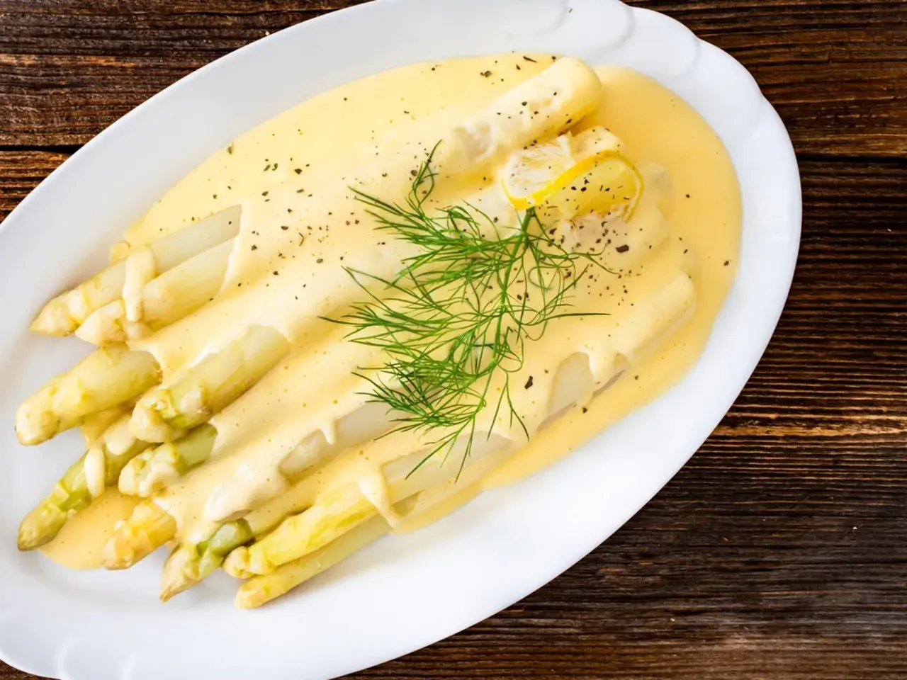 Frischer weißer Spargel mit cremiger Hollandaise, garniert mit Dill und Zitronenscheiben. Ein Klassiker der Saison.