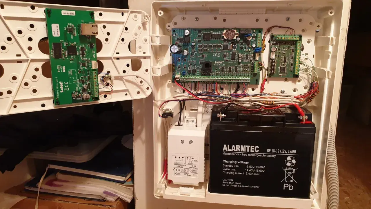 Wnętrze centrali alarmowej Satel z modułem ETHM-1 Plus, płytą główną Integra i akumulatorem.