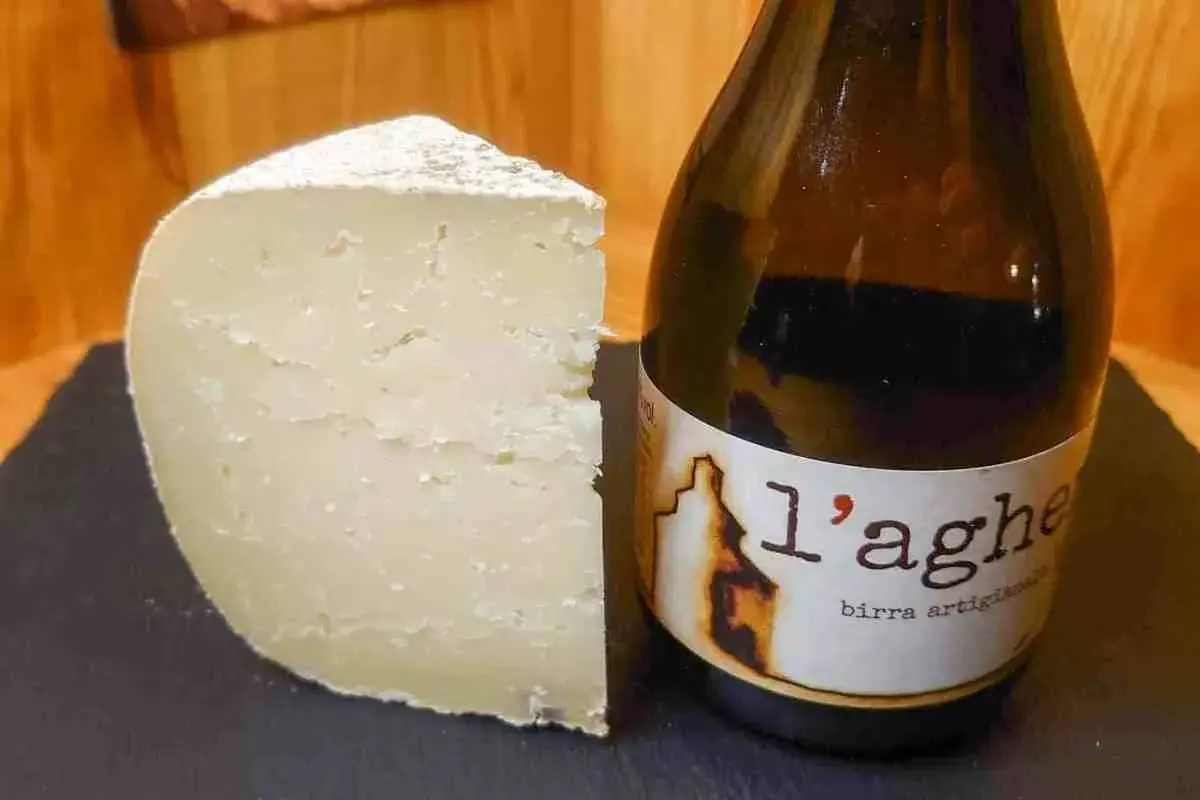 Un pezzo di formaggio stagionato accanto a una bottiglia di birra artigianale. Un abbinamento perfetto di birra e formaggio.
