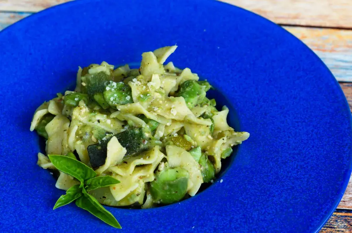 Pyszny makaron z bobem i cukinią, posypany parmezanem, podany na niebieskim talerzu.