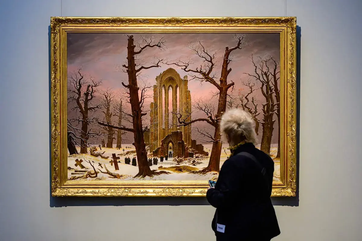 Besucherin betrachtet Caspar David Friedrichs "Abtei im Eichwald" in der Alten Nationalgalerie. Ein winterliches Motiv mit Ruinen und Kreuzen.