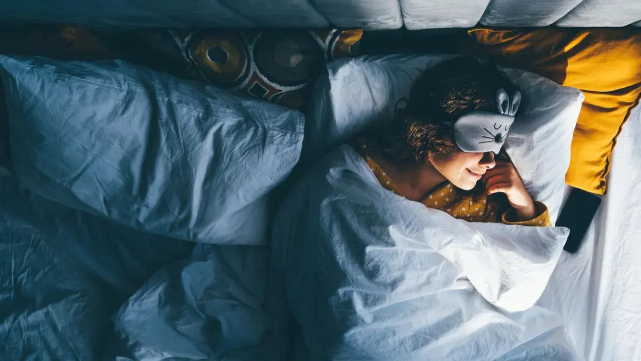 Ein Mädchen mit Hasen-Schlafmaske liegt im Bett und scheint schnell einschlafen zu wollen.