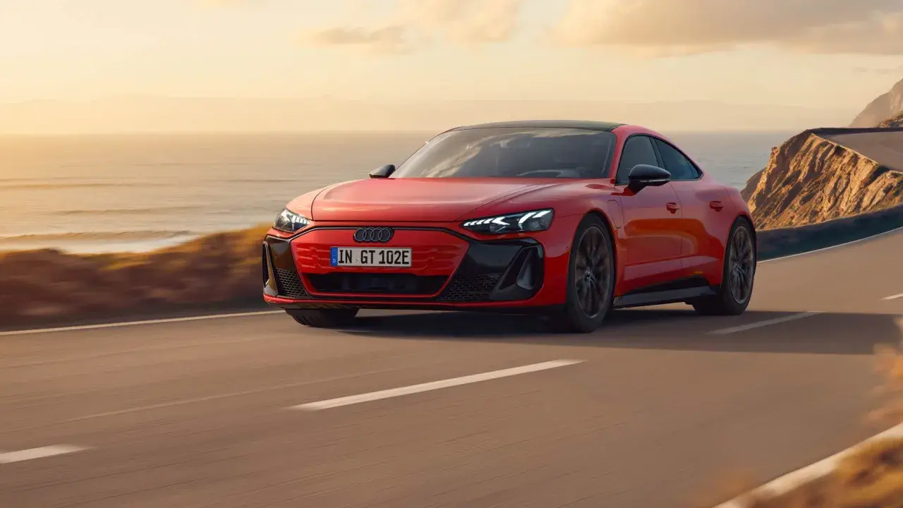 Czerwony Audi e-tron GT sunie po malowniczej nadmorskiej drodze o zachodzie słońca.