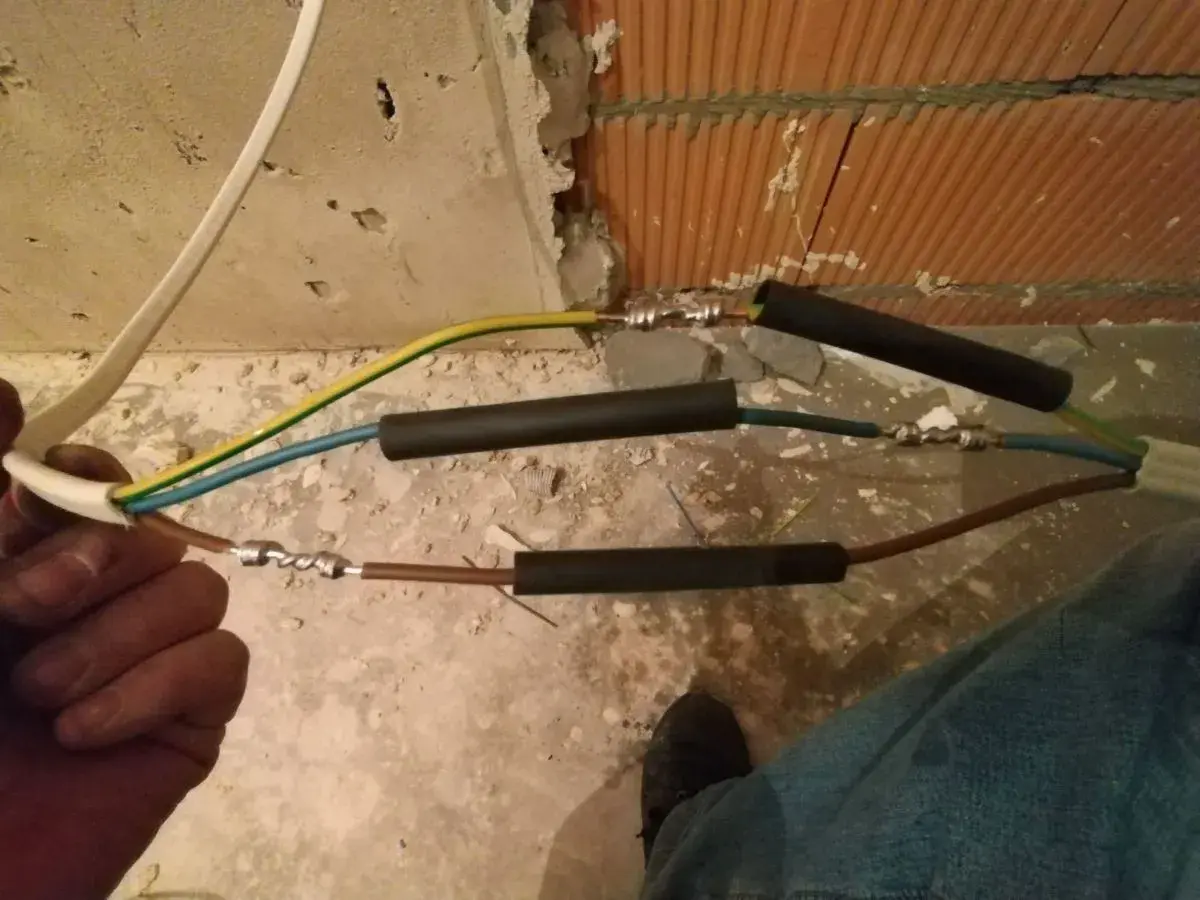 Ręczne skręcanie kabli elektrycznych, przygotowanie do izolacji. Widać połączenia przewodów w trakcie pracy.
