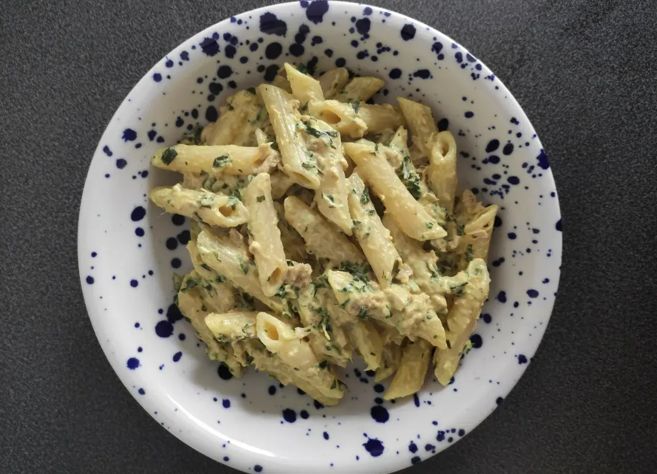 Penne z kremowym sosem, kawałkami tuńczyka i zieloną natką pietruszki, podane w talerzu w granatowe cętki.