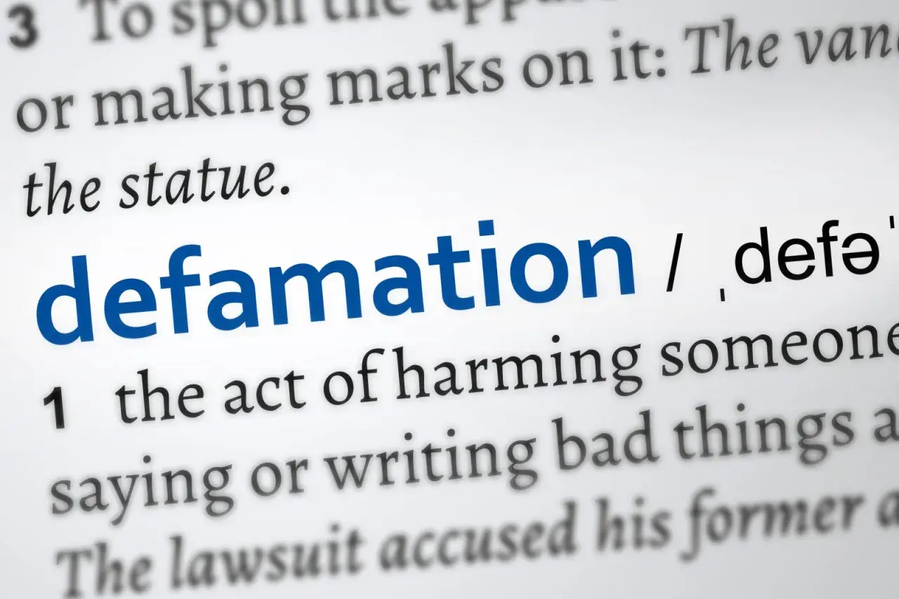 Słownikowa definicja "defamation" (zniesławienia), opisująca szkodzenie komuś przez mówienie lub pisanie złych rzeczy. Uważaj na pomówienia w pracy.