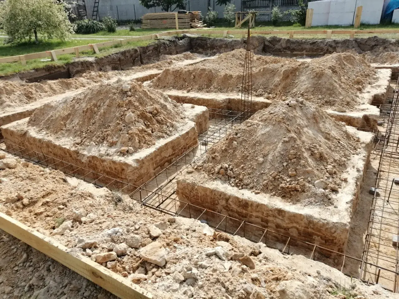 Wykop pod fundamenty bez szalunku, z widoczną zbrojeniem i usypaną ziemią.