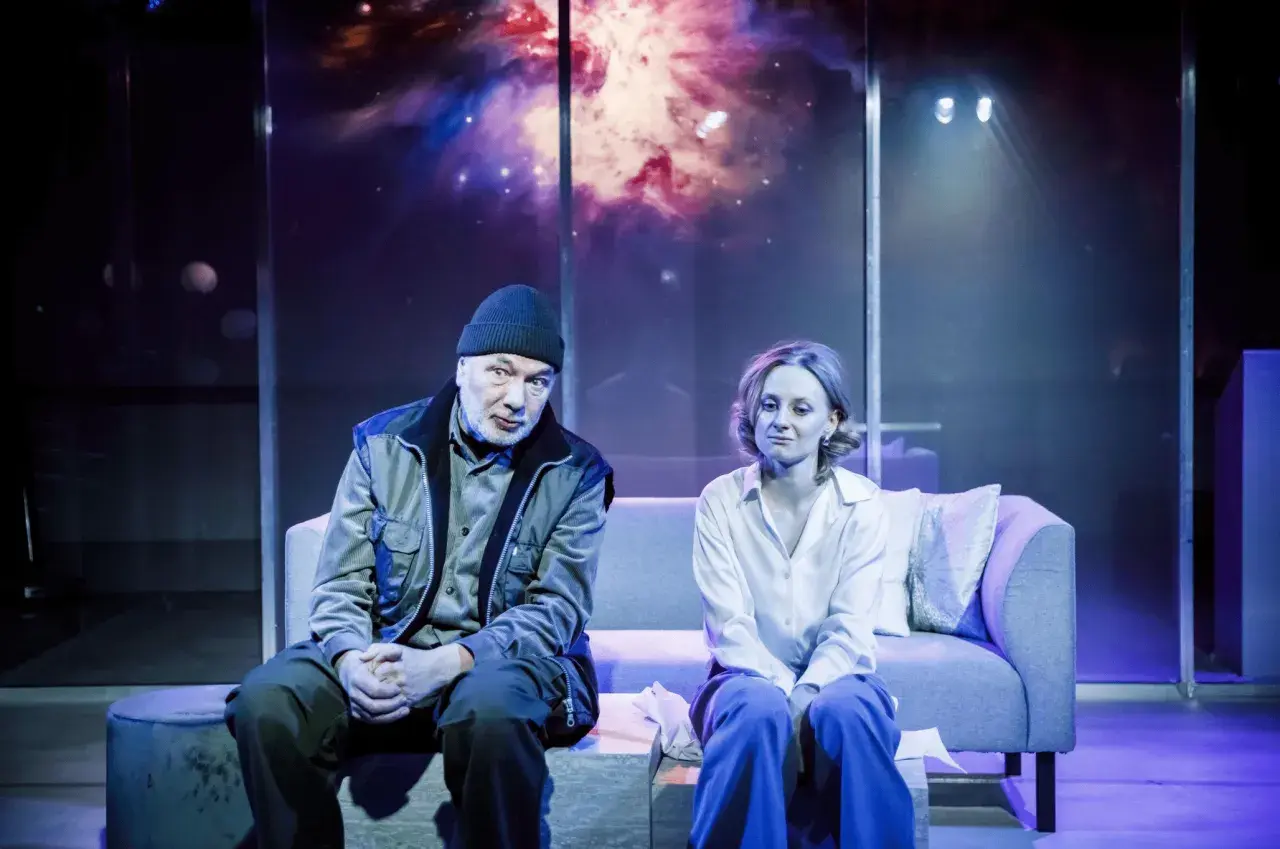 Para siedzi na kanapie w teatrze współczesnym na Mokotowie w Warszawie. Tło sceny to kosmiczna mgławica.