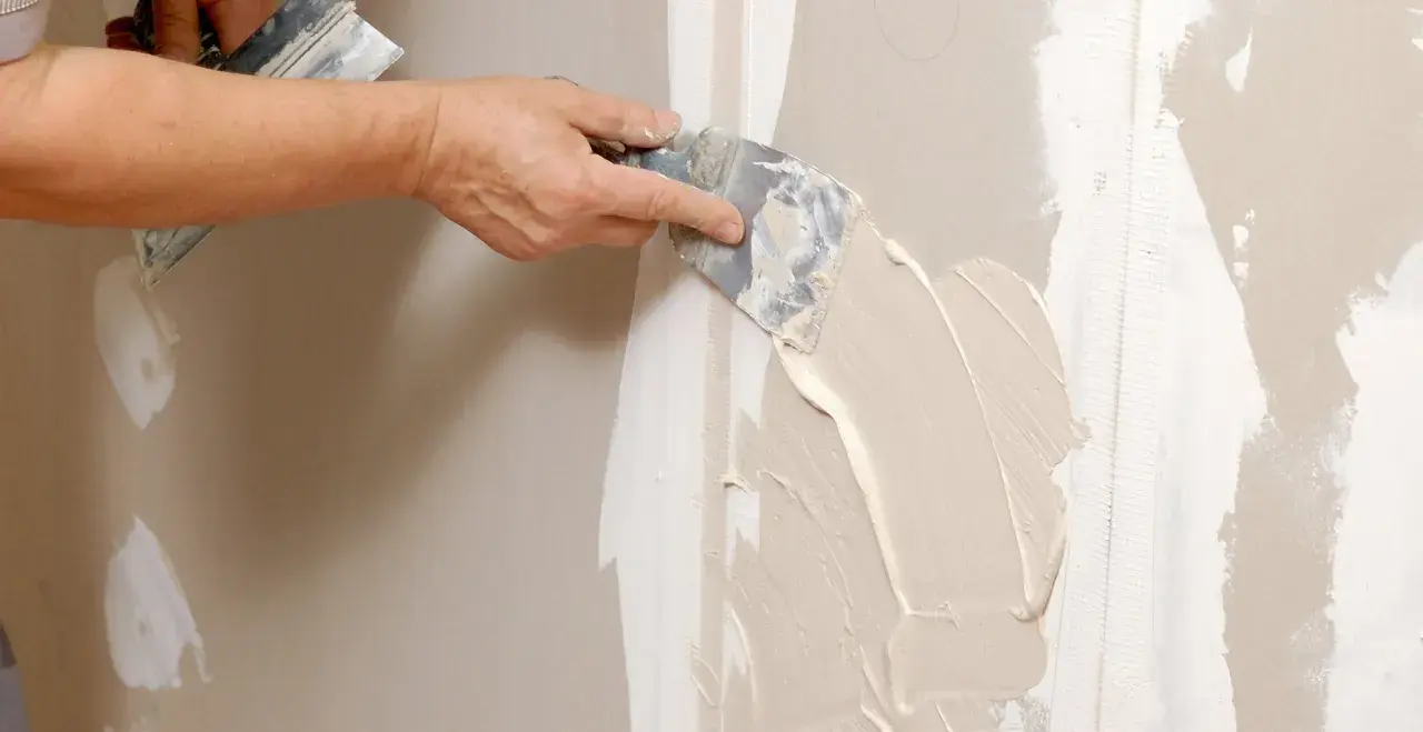 Mano stende stucco su una giuntura di cartongesso, ricordando che il cartongesso ha un verso.