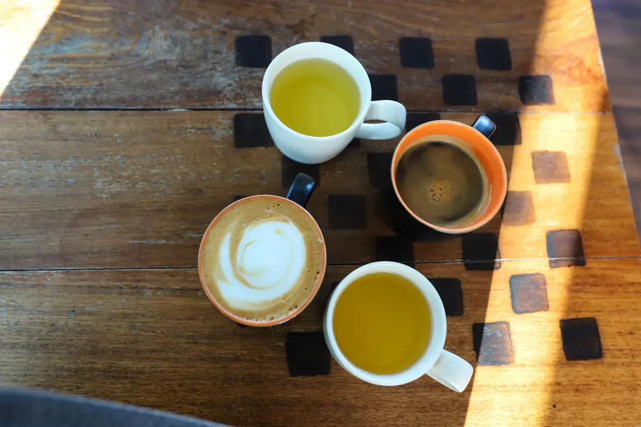 Kawa i herbata na drewnianym stole. Czy zielona herbata pobudza? Obok niej kawa latte i espresso.