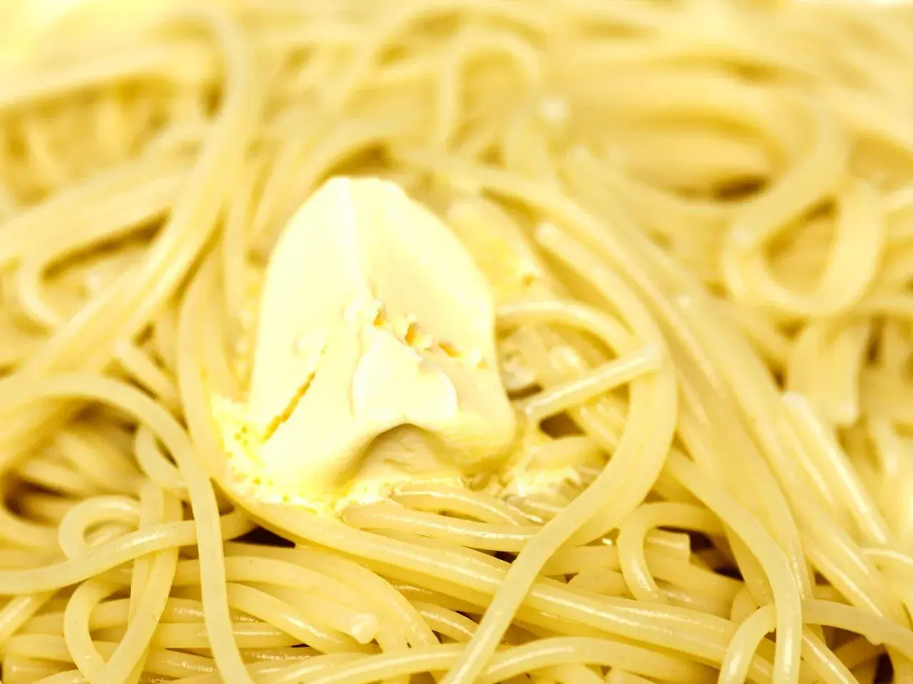 Un piatto di pasta in bianco, con spaghetti conditi da una generosa porzione di burro che si scioglie.