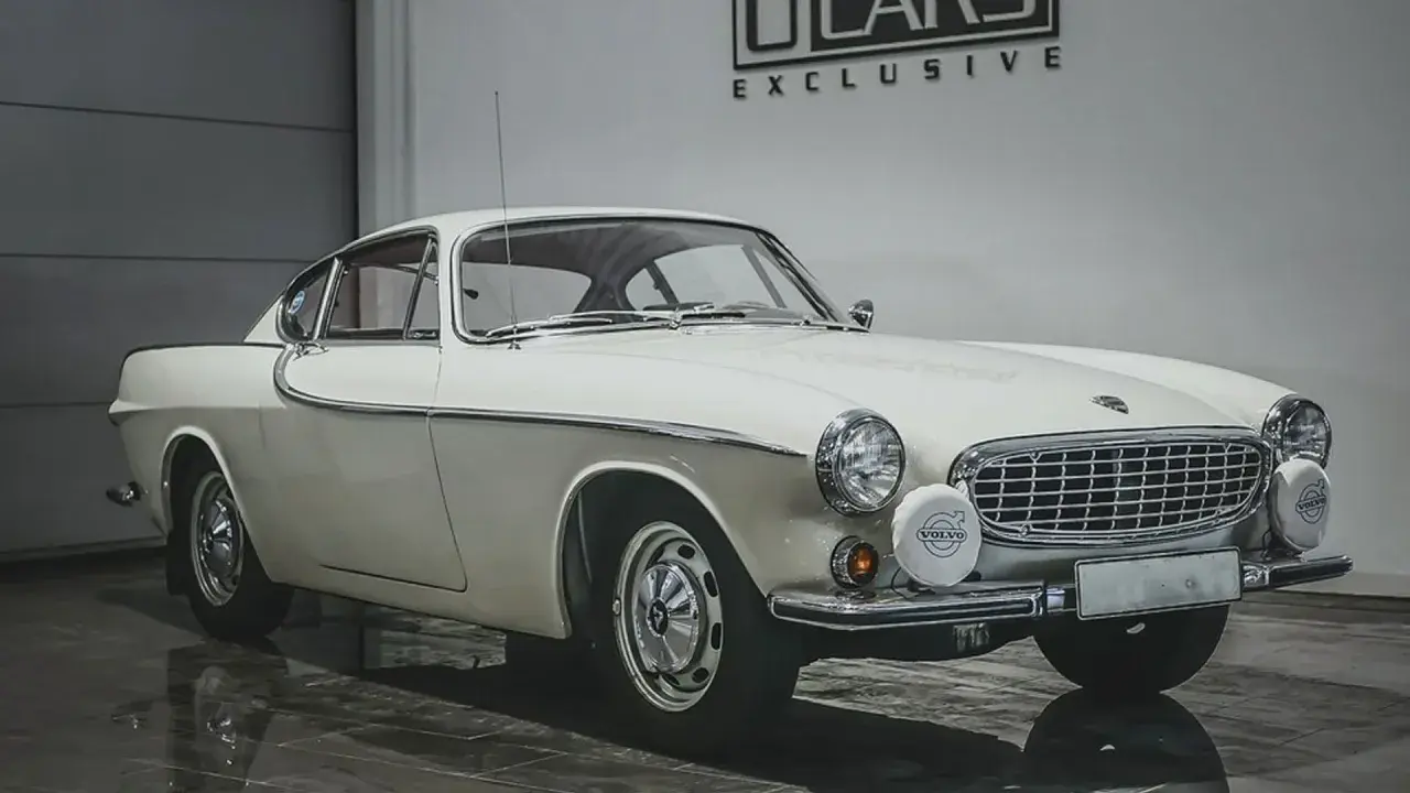 Vit Volvo P1800, en ikonisk bil som påminner om James Bond. Klassisk design med kromdetaljer och runda strålkastare.