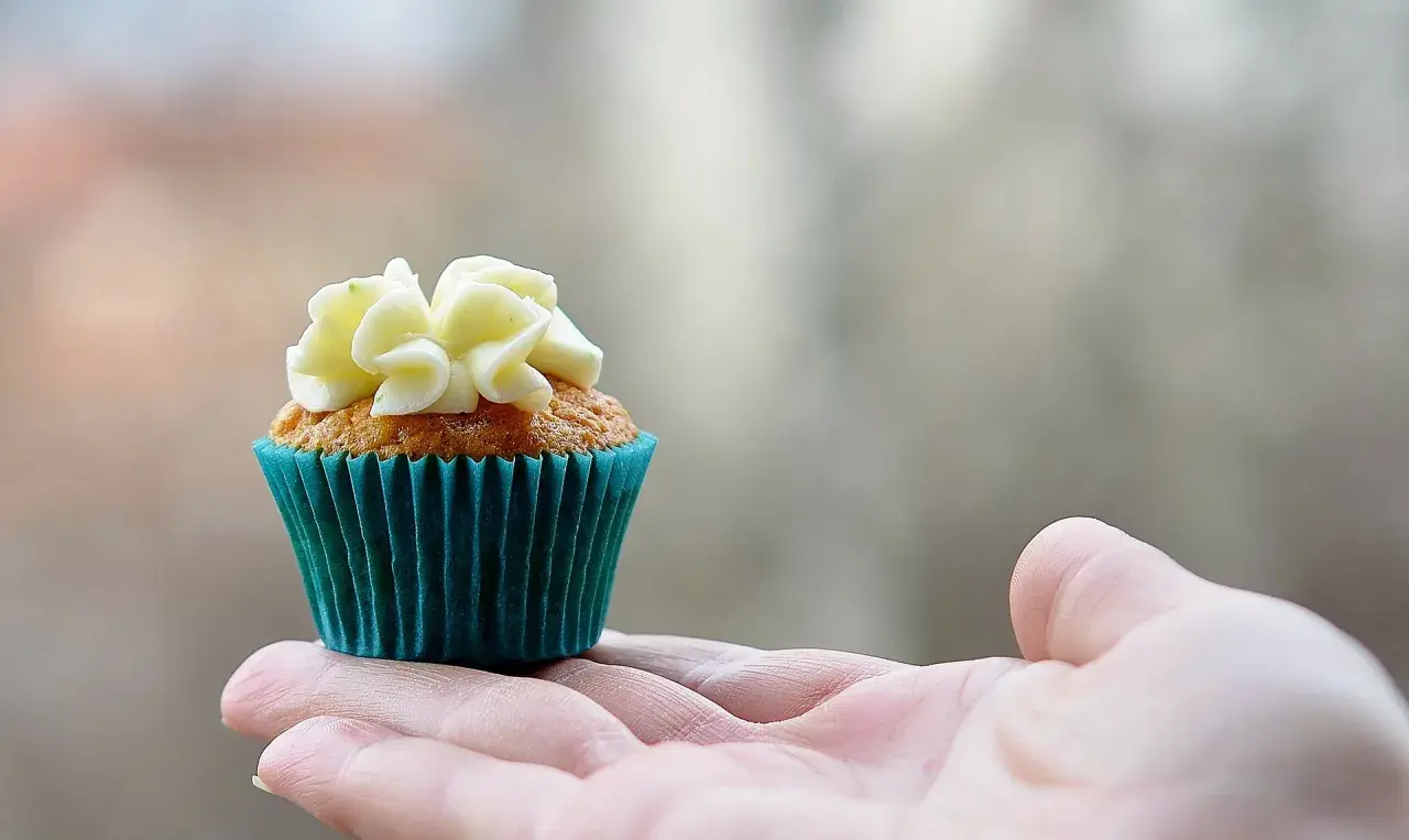 En hand håller en saftig muffins med vit frosting.