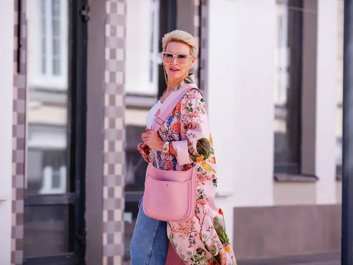 Kobieta w kwiecistym kimonie w stylu Moschino Bubble Gum, z różową torebką i okularami, idzie ulicą.