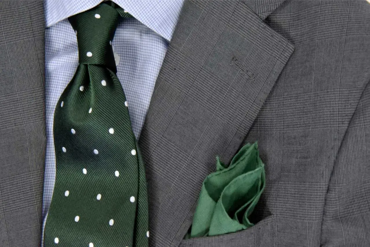 Elegancki zestaw: niebieska koszula, zielony krawat w kropki i szara marynarka w kratę. Idealna odpowiedź na pytanie: jaki krawat do niebieskiej koszuli.