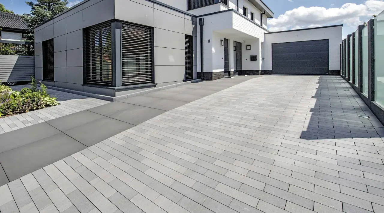 Moderne Einfahrt pflastern mit grauen Steinen. Das Haus hat eine graue Fassade und weiße Akzente.