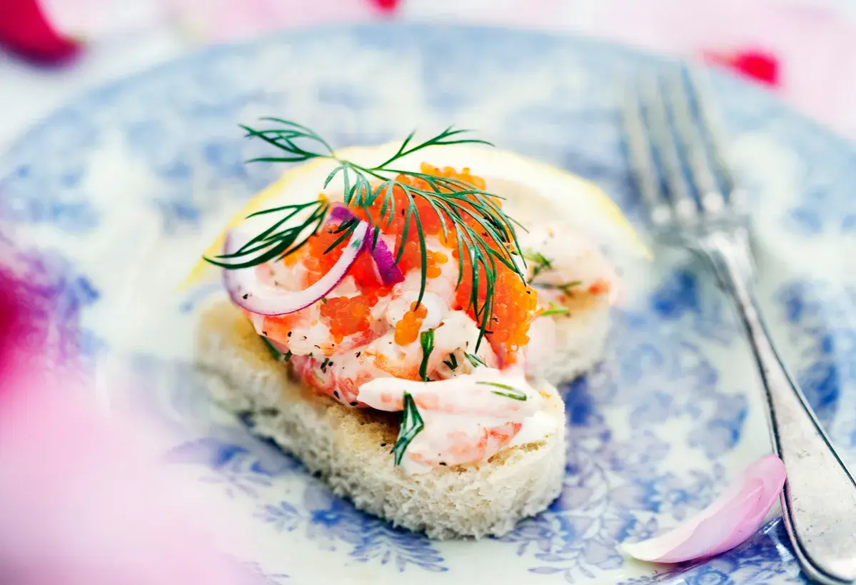 En läcker toast Skagen med räkor, rom, dill och rödlök på en blåvit tallrik.