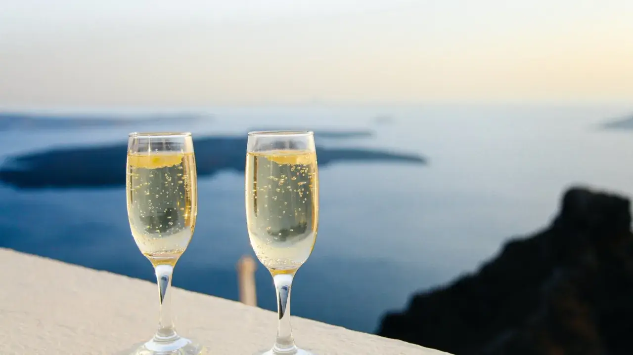 Zwei Gläser Champagner mit Bläschen vor einer Meereslandschaft. Die Frage, wie lange ist Champagner haltbar, beschäftigt Genießer.