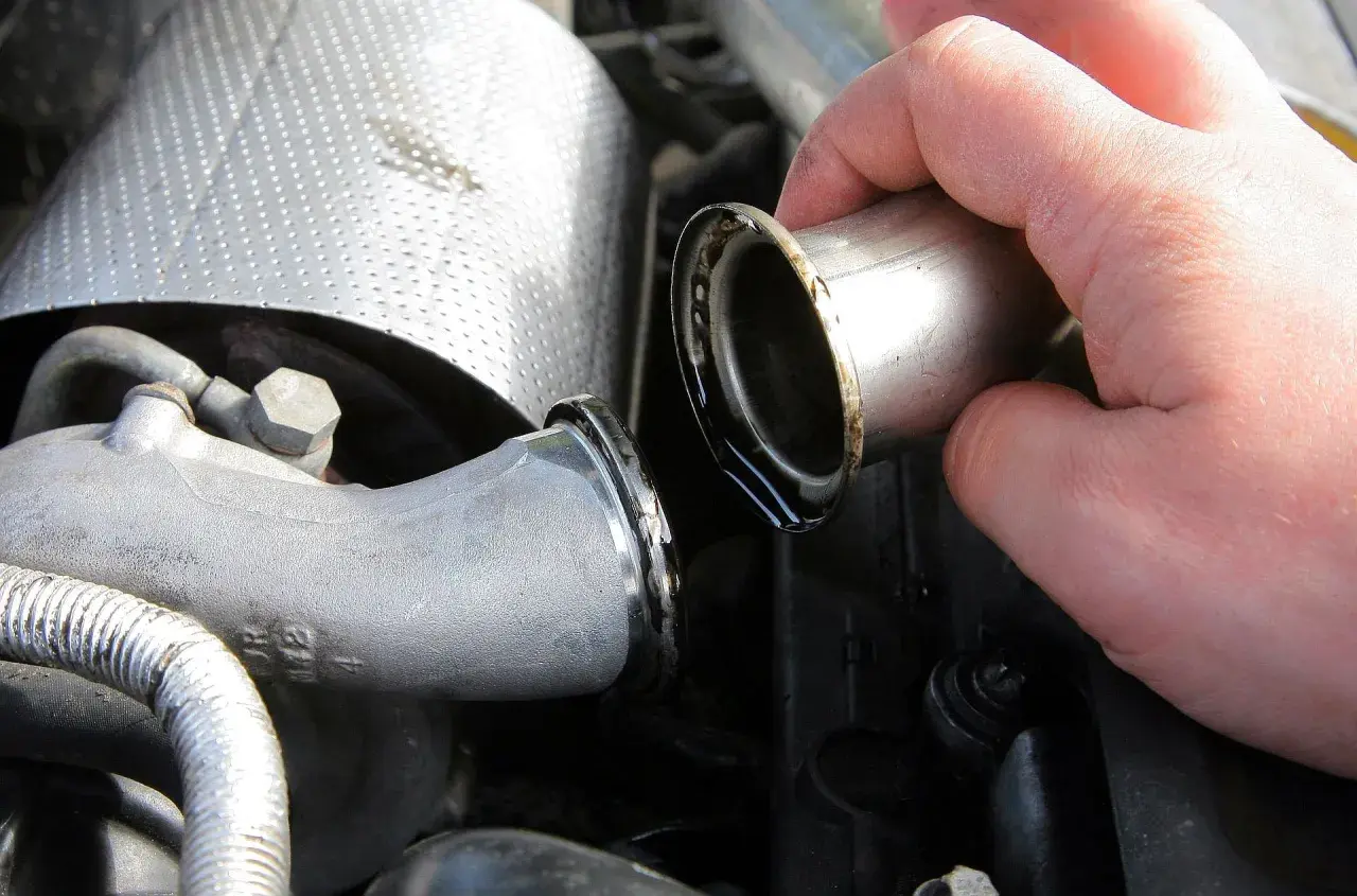 Dłoń trzymająca metalową rurkę z widocznymi śladami oleju, część układu dolotowego turbiny auto.