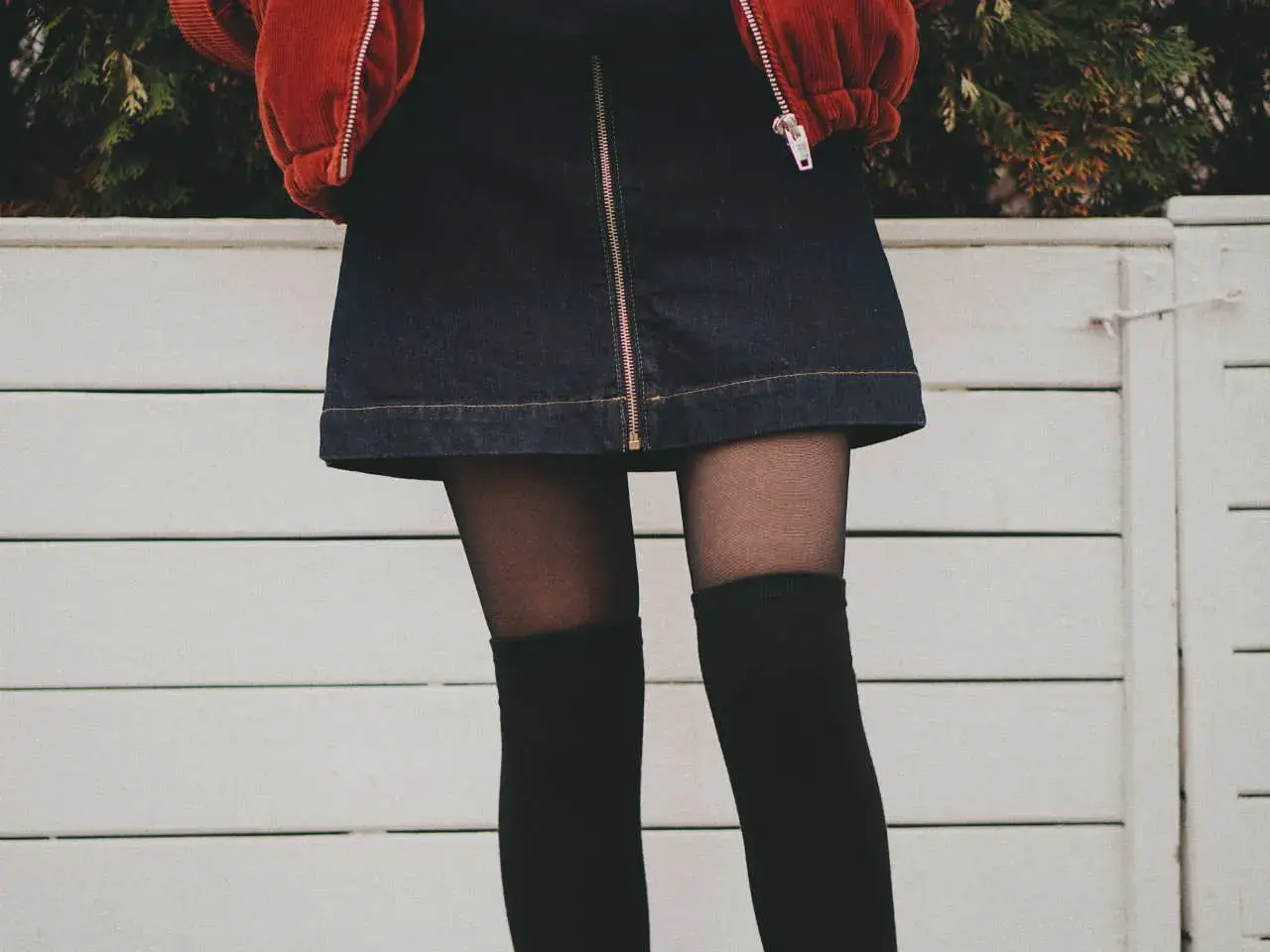 Stylowy outfit z dżinsową spódniczką, czarnymi zakolanówkami i pomarańczową kurtką.