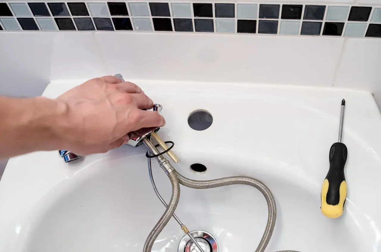 Hand montiert einen Wasserhahn, um das Waschbecken zu reparieren. Ein Schraubenzieher liegt bereit.