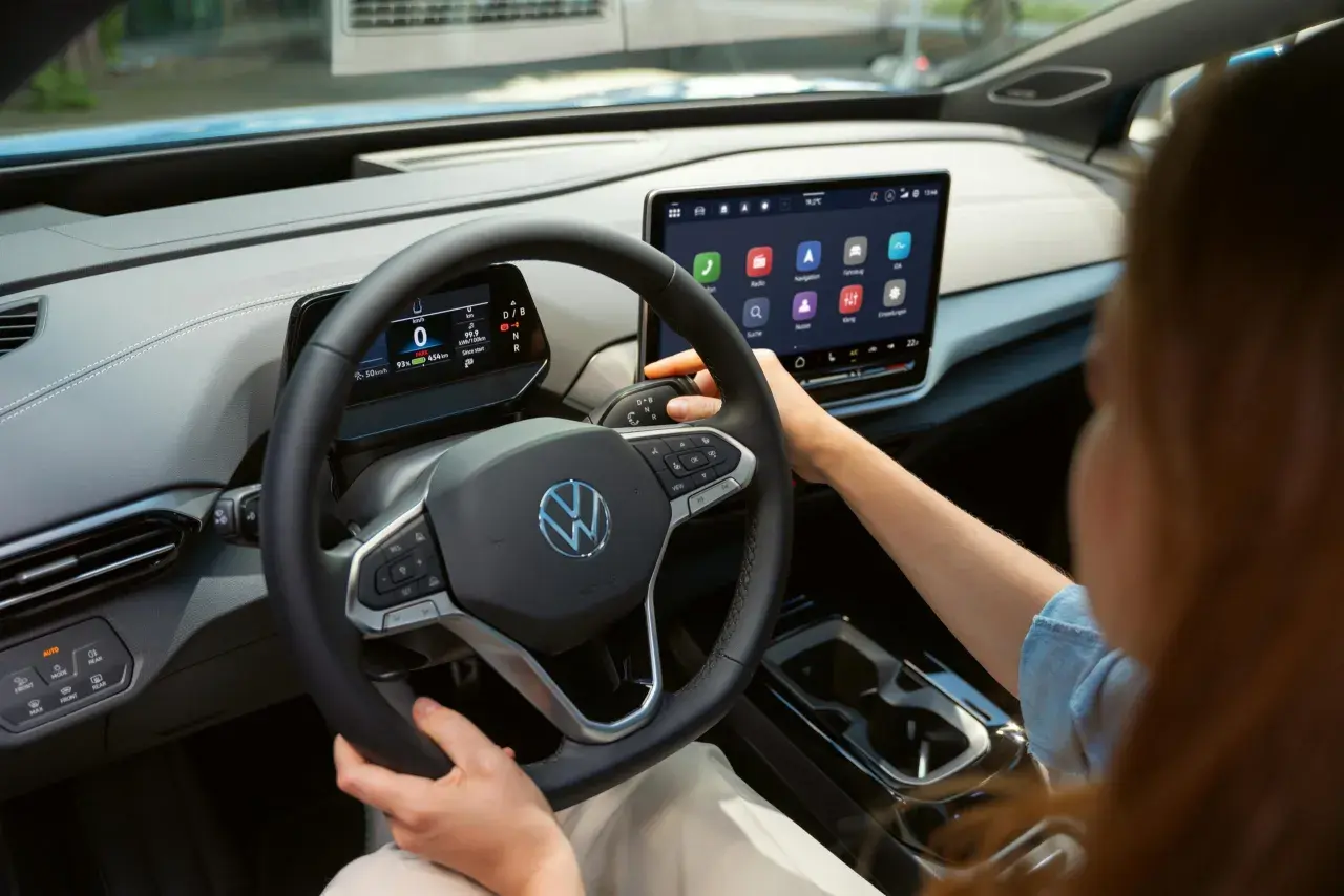 Interior de un coche eléctrico Volkswagen. Se ve el volante, la pantalla táctil central y la palanca de cambios. La dirección asistida progresiva se adapta a la velocidad.