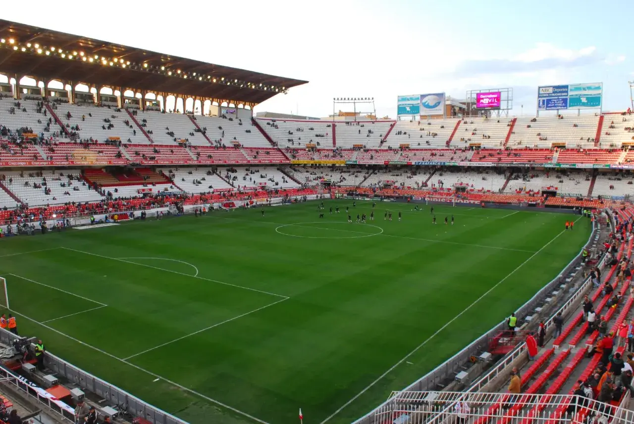 Piłkarze rozgrzewają się na murawie stadionu Sevilla. Widownia zajmuje miejsca na czerwono-białych trybunach.
