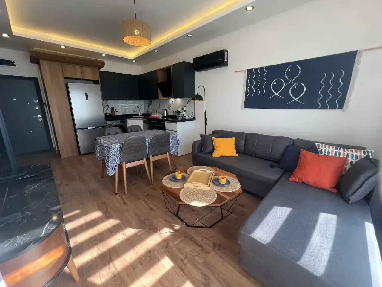 Nowoczesny salon z aneksem kuchennym, idealny na najem krótkoterminowy. Sofa, stolik kawowy, jadalnia i kuchnia.