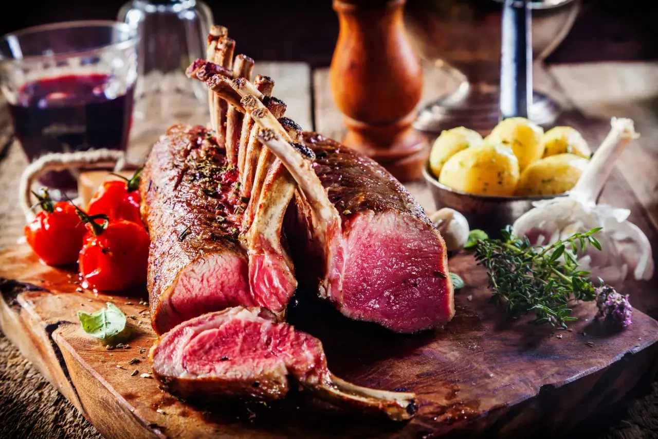 Un succulent carré d'agneau rôti, accompagné de tomates cerises, de pommes de terre et d'une touche d'herbes fraîches.