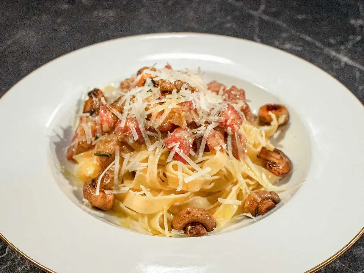En tallrik med pasta alla boscaiola, toppad med riven parmesan och champinjoner.
